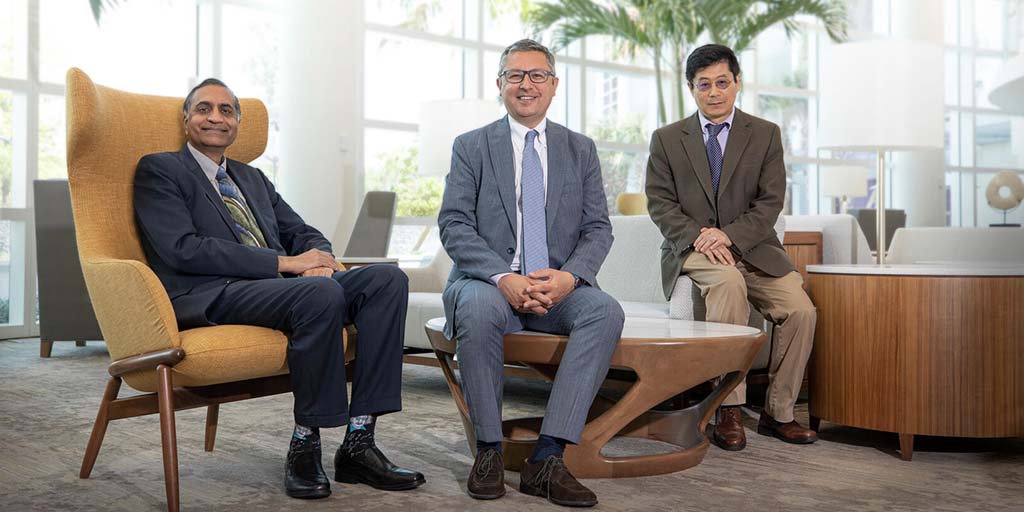 Three male physicians wearing business suits sitting in a modern waiting room, looking at camera.