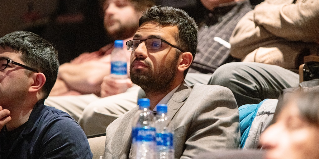 Medical student attending Medical Grand Rounds presentation and listening in crowd