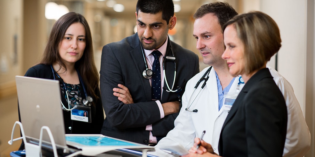 Group of four students and faculty looking at computer station in hallway of hospital