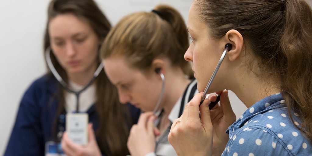 Three women with stethoscopes listening to heart simulation during training