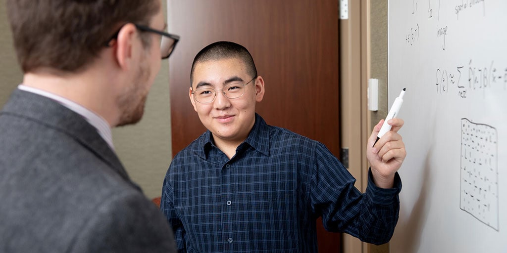 Student at a whiteboard pointing to something and showing teammate