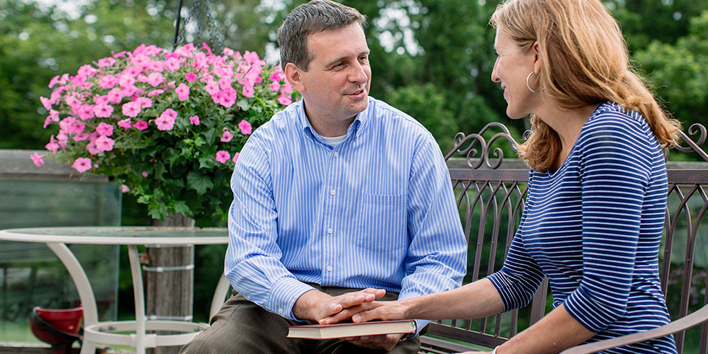 A hospital chaplain sits on a park bench and provides spiritual counseling to a woman