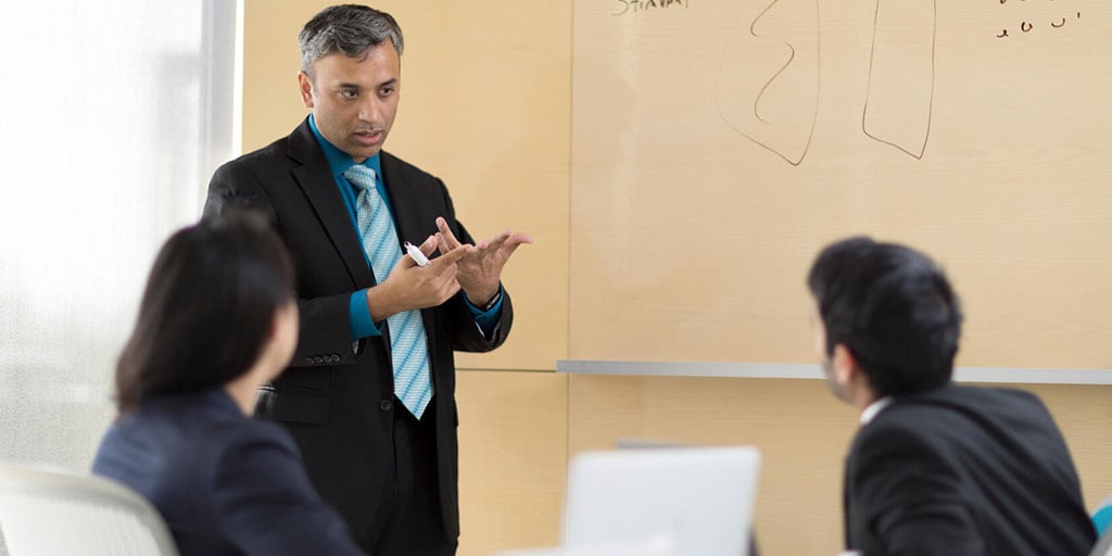 Faculty member at the head of the classroom, in front of a white board, providing lecture to two students