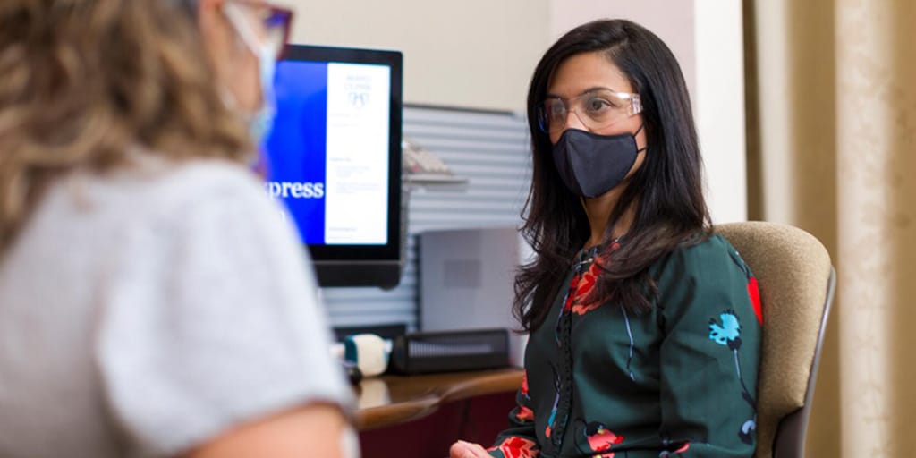 Nurse practitioner sitting at a computer, facing a patient in an exam room