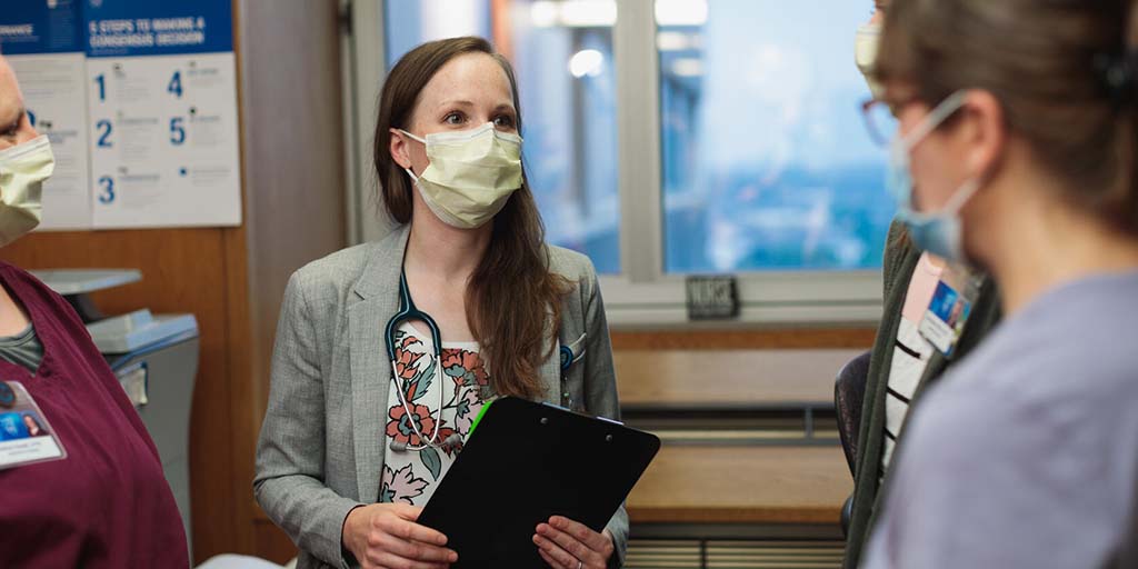 Group of people standing in a hallway in a hospital making rounds, and discussing patient cases.