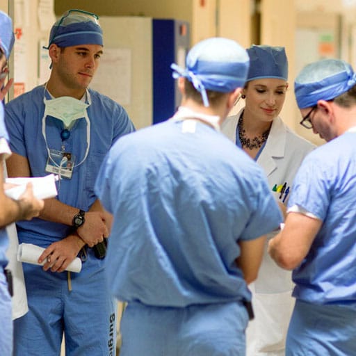 Group of 8 people wearing surgery scrubs in a hallway discussing something on a clipboard