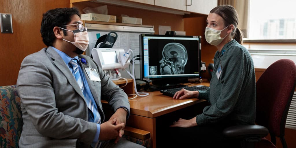 Health care provider sitting at a desk next to patient reviewing a scan on a computer