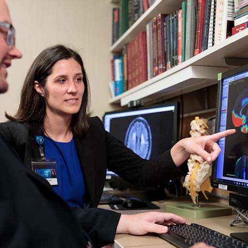 Fellow and patient sitting at a desk looking at an MRI brain scan on a desktop computer