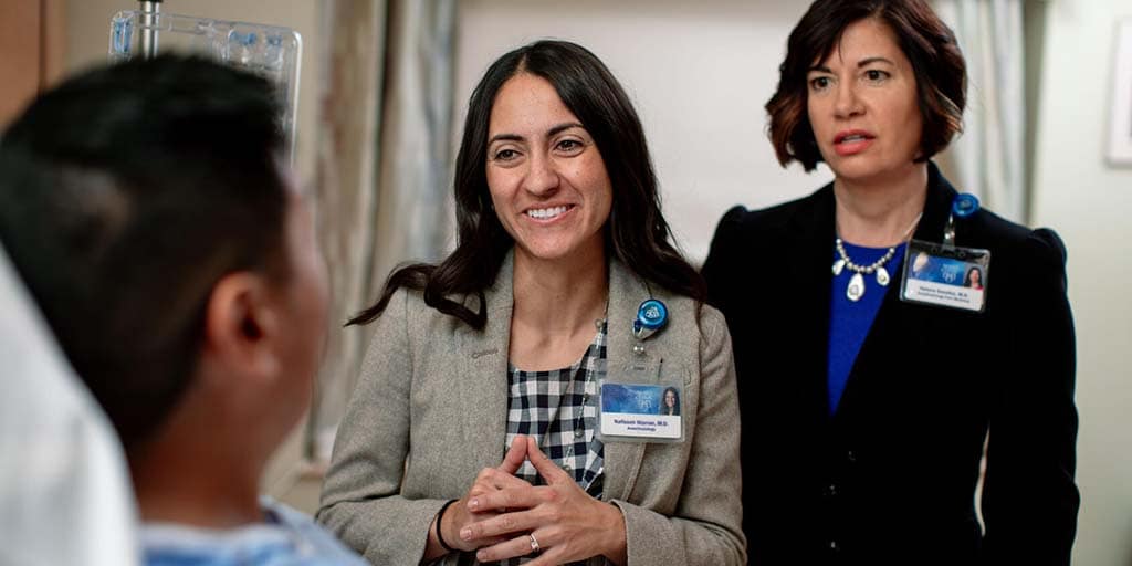 Solid organ transplant physician and fellow meet with a patient in an exam room