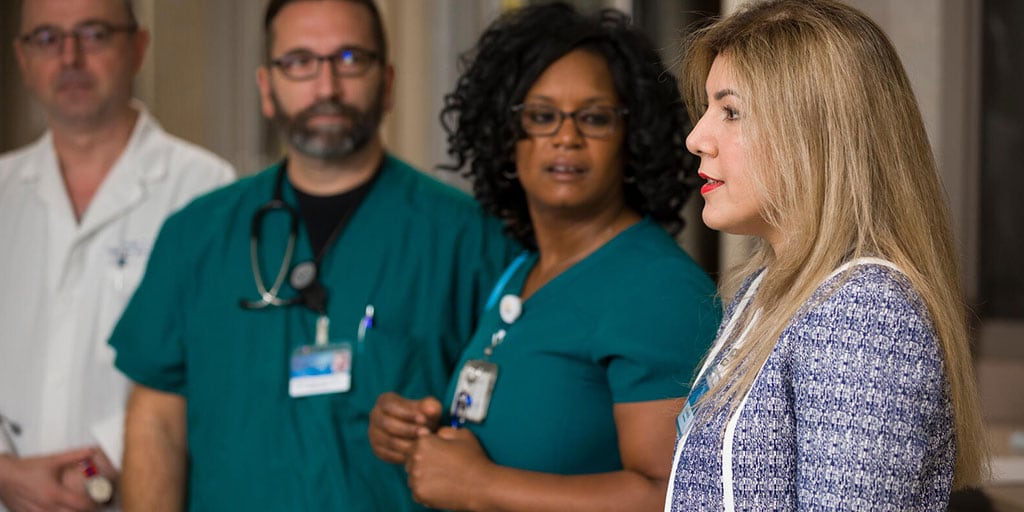 Three members of the health care staff standing in a line, looking at one member who is discussing their point of view.