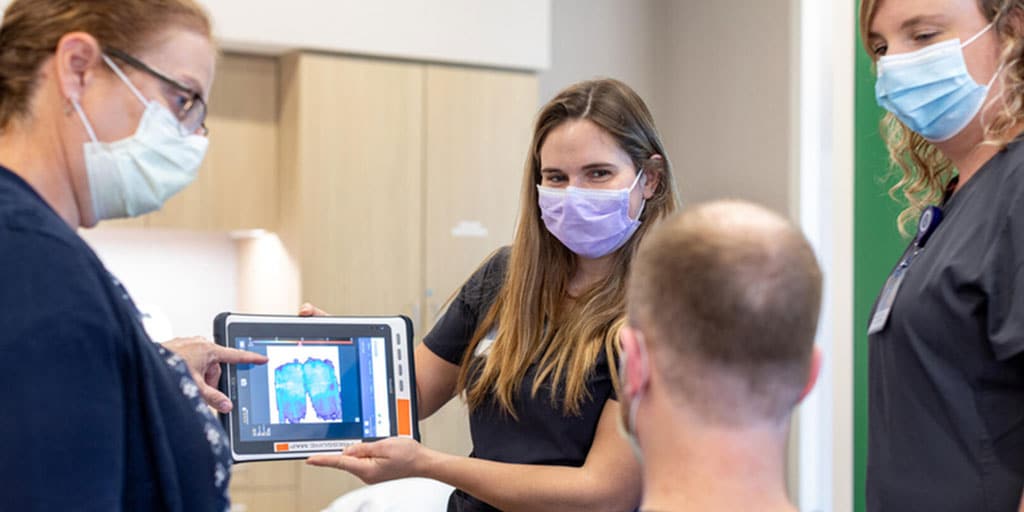 Group of three physical therapists showing a patient something on an ipad