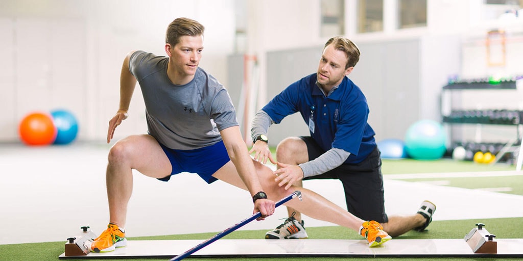 Physical therapist assisting hockey player with side lunges and knee rehab