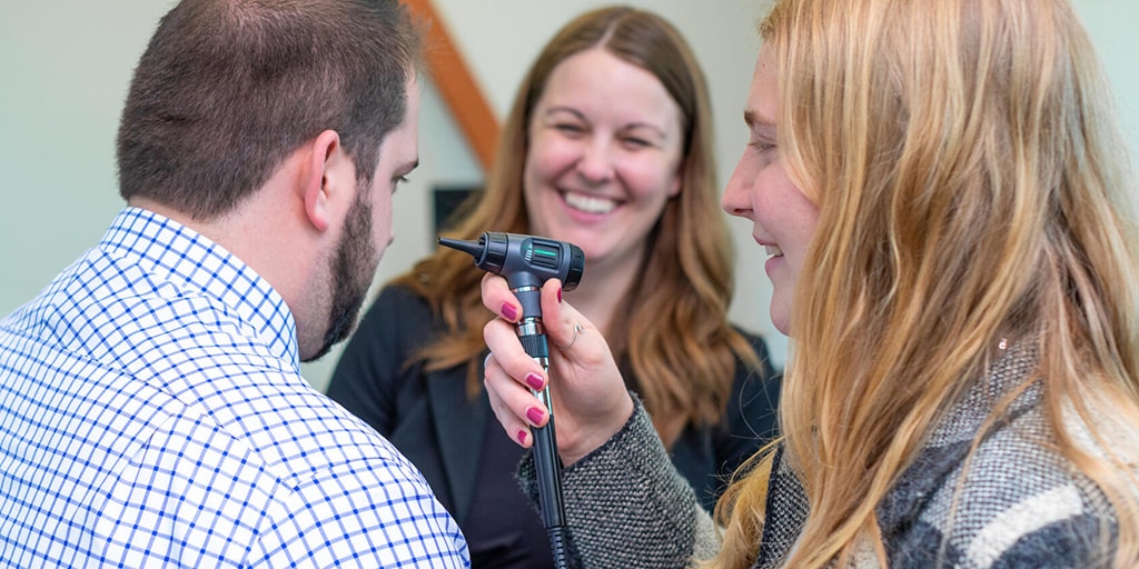 Physician assistants (PA) use an otoscope to examine a patient's ear.