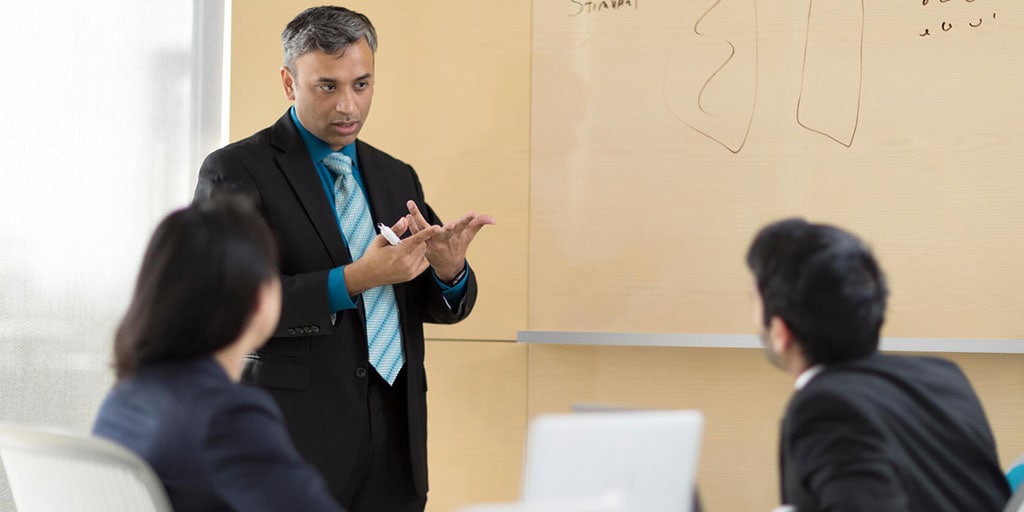 Faculty member at the head of the classroom, in front of a white board, providing lecture to two students