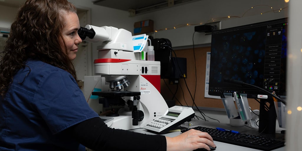 Molecular pathology technician reviews molecular images on the microscope and computer in the lab