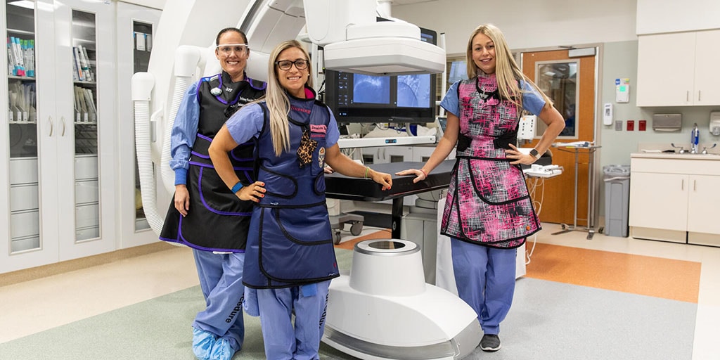 Three Mayo Clinic technicians stand next to a C-arm imaging device.