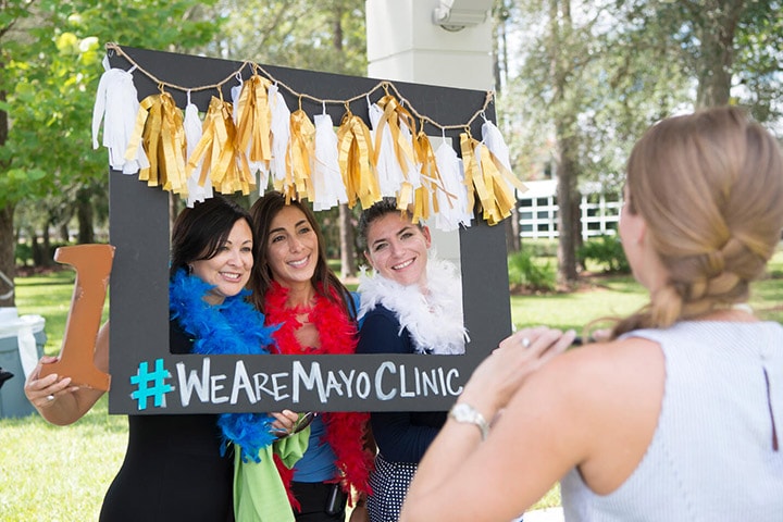 Mayo Clinic employees pose for a group photo behind a decorated frame that includes the hashtag #WeAreMayoClinic