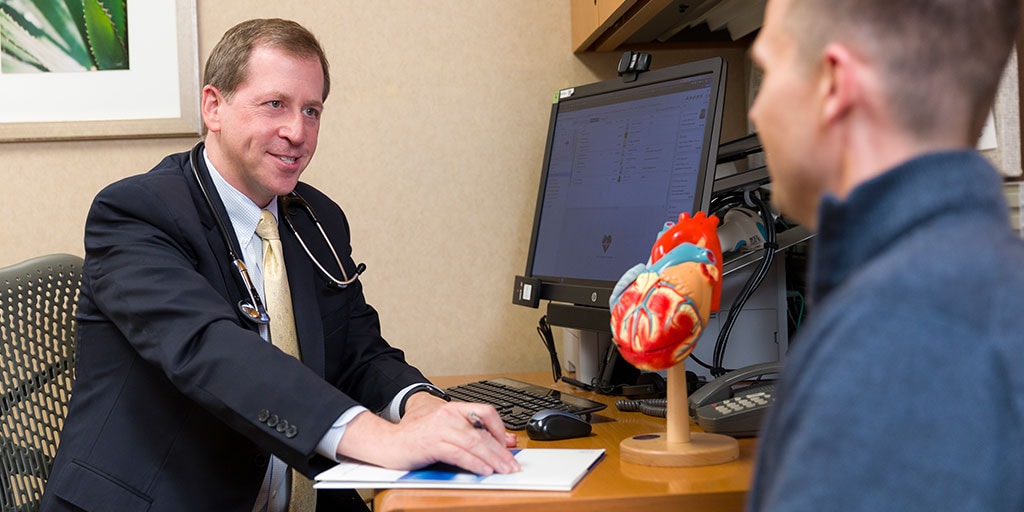 Cardiovascular physician sitting in front of a computer with a patient discussing something on the computer