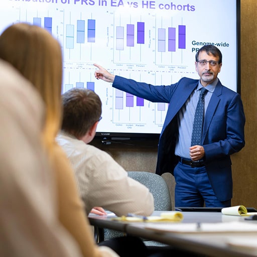 The program director from the Cardiology, Genomics Fellowship in Rochester, Minnesota, at Mayo Clinic School of Graduate Medical Education stood in front of a room and gave a lecture while pointing at the coinciding information on the digital presentation board.