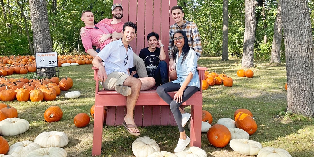 Six people sitting on a giant Adirondack chair in the middle of a pumpkin patch