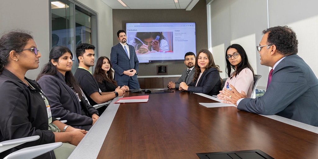 Nine people from the Critical Care Medicine Fellowship program at Mayo Clinic in Jacksonville, Florida, had a discussion during a presentation in a conference room.