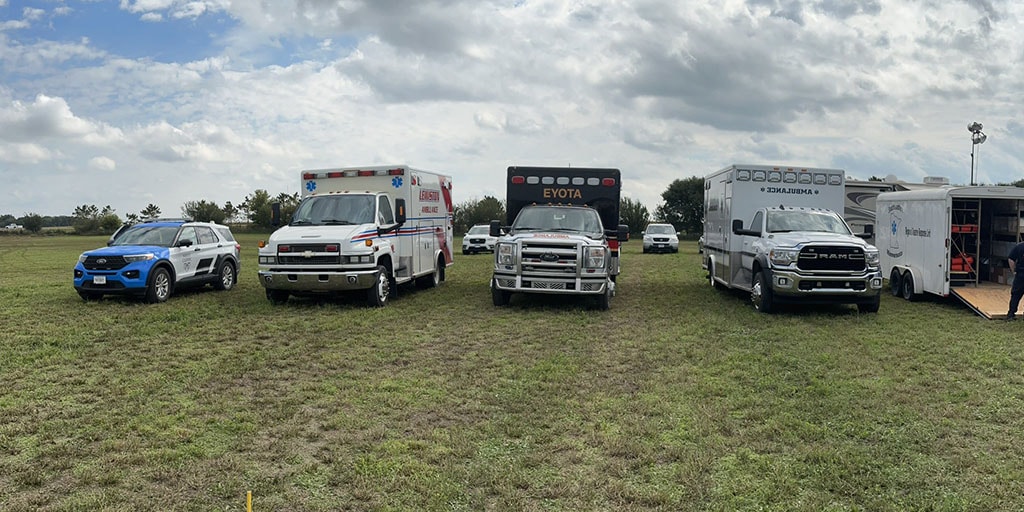 Several ambulance and emergency vehicles parked in a line in a field.