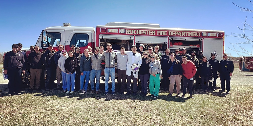 Group picture of the Rochester Fire Department in front of a fire truck in a field