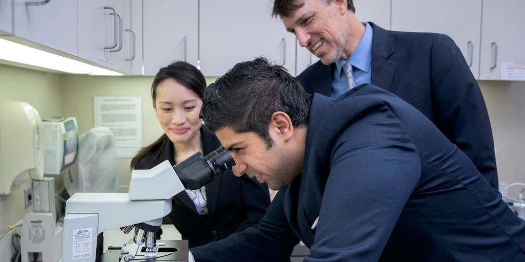 Family medicine residents and a faculty member look at a sample under a microscope.