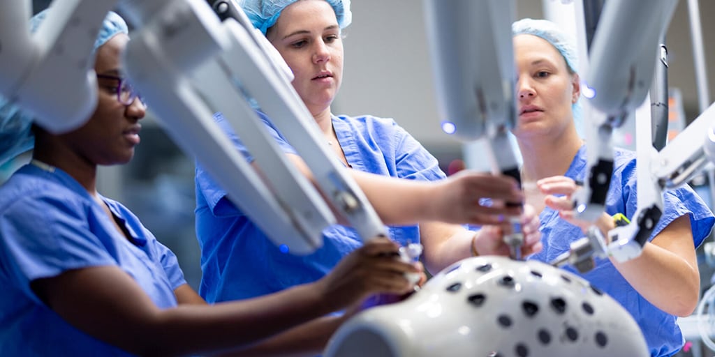 Three doctors use a machine to practice a procedure.