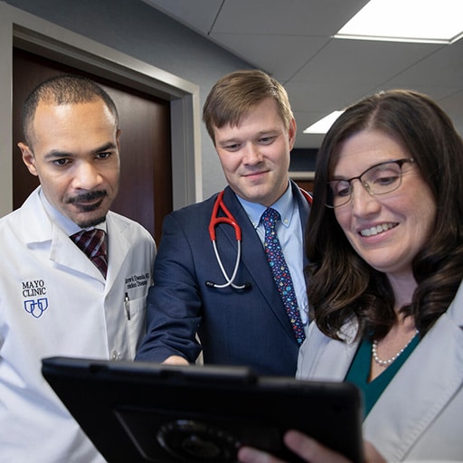 Three doctors from the Infectious Diseases Fellowship at Mayo Clinic in Jacksonville, Florida, have a discussion in hall way while viewing a tablet.