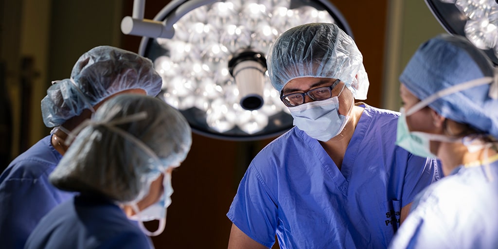 Four doctors dressed in medical attire perform a procedure in an operating room.