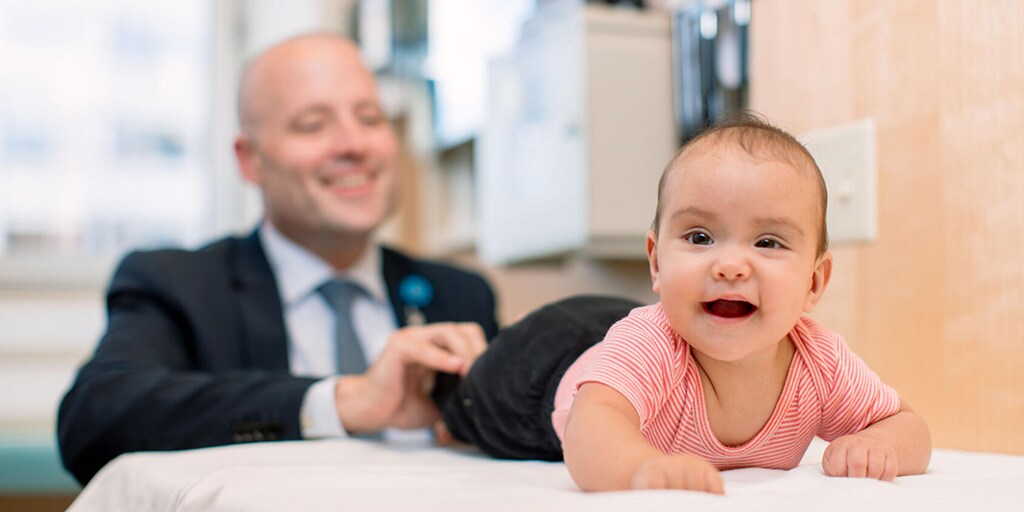 A doctor checks the foot reflexes of a baby on an exam table.