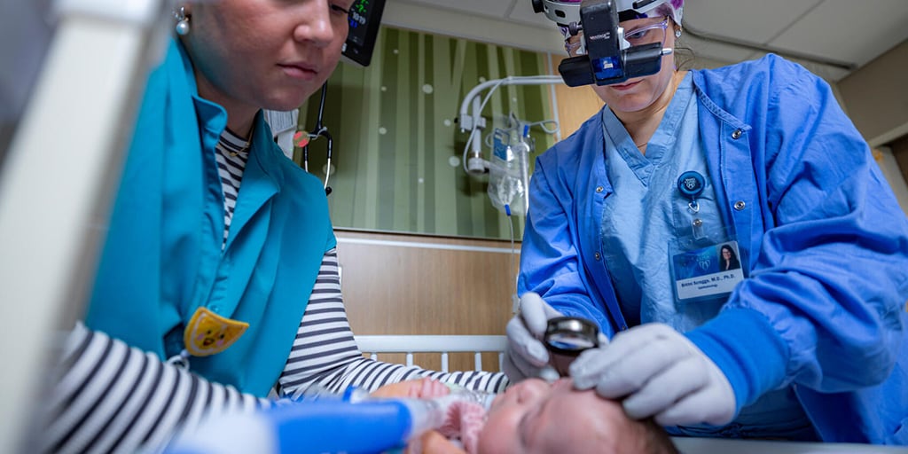 Two doctors in the ICU examine a newborn baby.