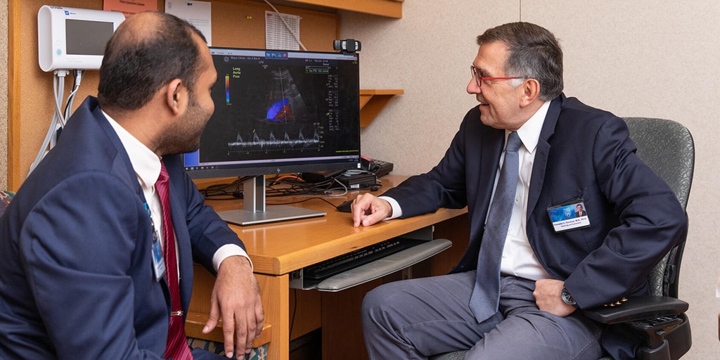 Physicians seated in an examination room discuss the results of a scan on the computer monitor beside them.