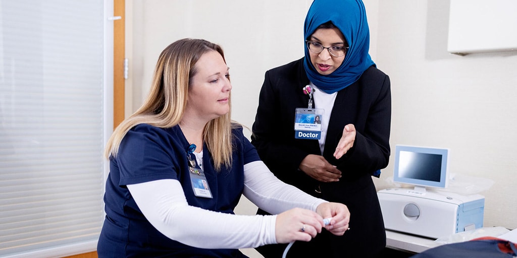 M. Salman Sheikh, MD, Nephrology fellow, discusses an out-of-frame patient's at-home dialysis machine with a nurse at the patient's bedside.