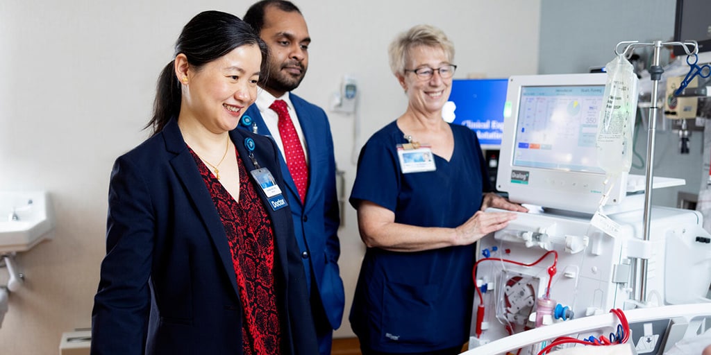 Nephrology fellows and a nurse speak to a dialysis patient at her bedside.