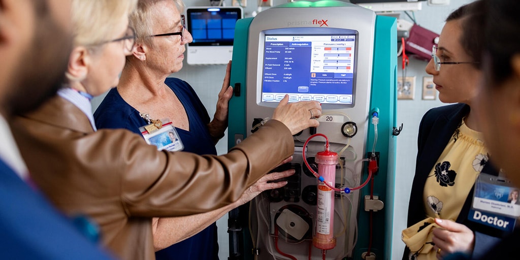 Iasmina Craici, MD, Nephrology consultant and fellowship program director, adjusts a touch-screen on a dialysis machine while other medical staff members observe.