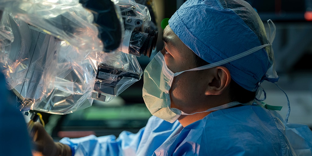 Neurologic surgery fellowship doctor in scrubs looking through microscope
