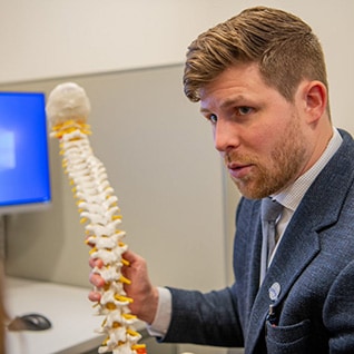 Physical Medicine and Rehabilitation Residency doctor providing an explanation while holding a human spine model.
