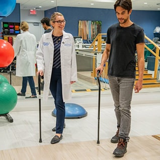 Physical Medicine and Rehabilitation Residency doctor walks alongside a patient in a rehabilitation room.