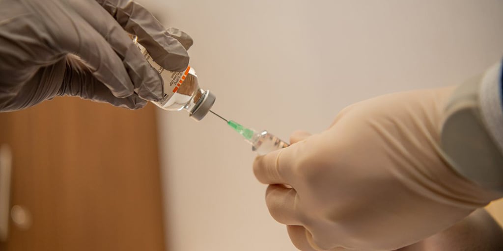 Demonstration of hands using a syringe with a needle to withdraw liquid from vial.