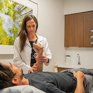 A doctor examines a patient's forearm in an exam room.