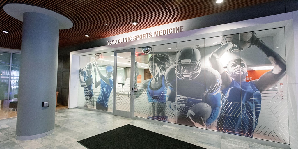 Glass wall mural of athlete images inside of Mayo Clinic Square building in Minneapolis, MN.