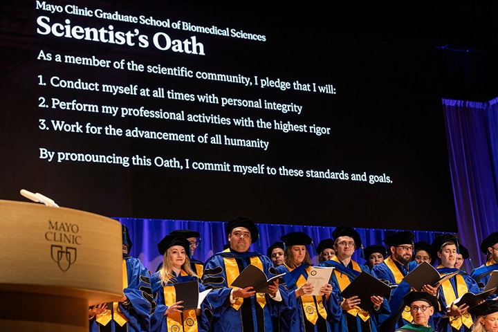 The Scientist's Oath shows on a large display behind rows of graduating Ph.D. students at Mayo Clinic